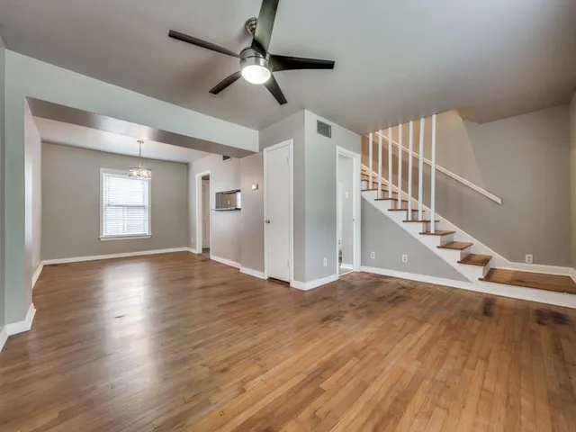 a view of an empty room with wooden floor and a ceiling fan