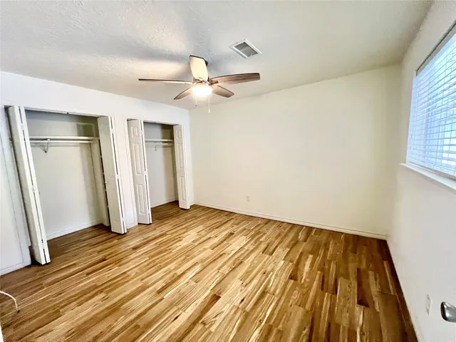 an empty room with wooden floor fan and windows
