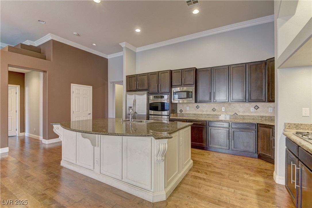 972 Rue Grand Paradis Lane Henderson, NV 89011 - Photo 6 of 32 Dual tone kitchen featuring two tone cabinetry, ornamental molding, dark stone counters, light wood-style flooring, and decorative backsplash