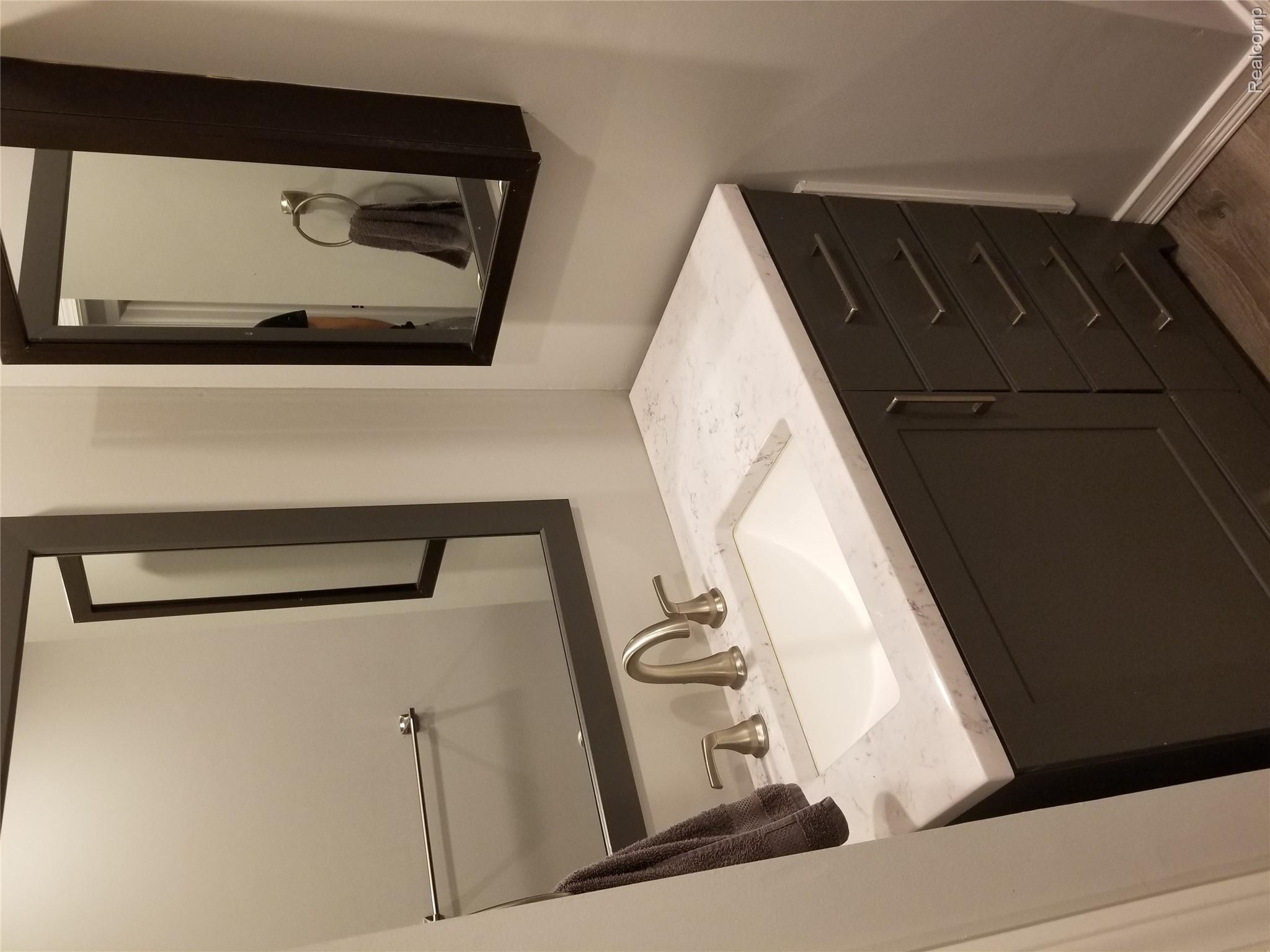 3231 West Utica Road Utica, MI 48317 - Photo 14 of 20 Vanity featuring a built-in rectangular sink with a two-handle faucet, solid surface countertop, and dark wood-finish cabinetry