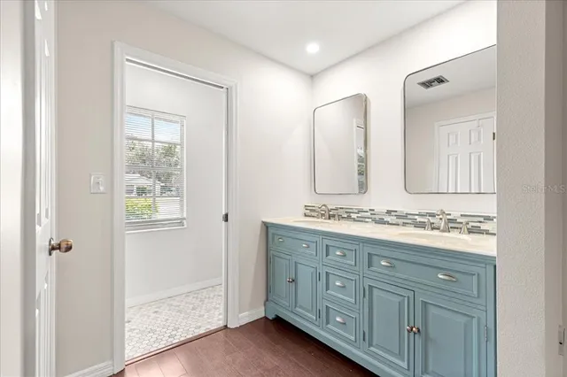 a bathroom with a double vanity sink and mirror with wooden floor