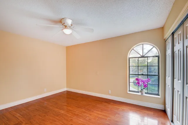 an empty room with wooden floor chandelier fan and windows