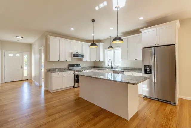 a kitchen with stainless steel appliances granite countertop a refrigerator a sink dishwasher a stove and white cabinets with wooden floor