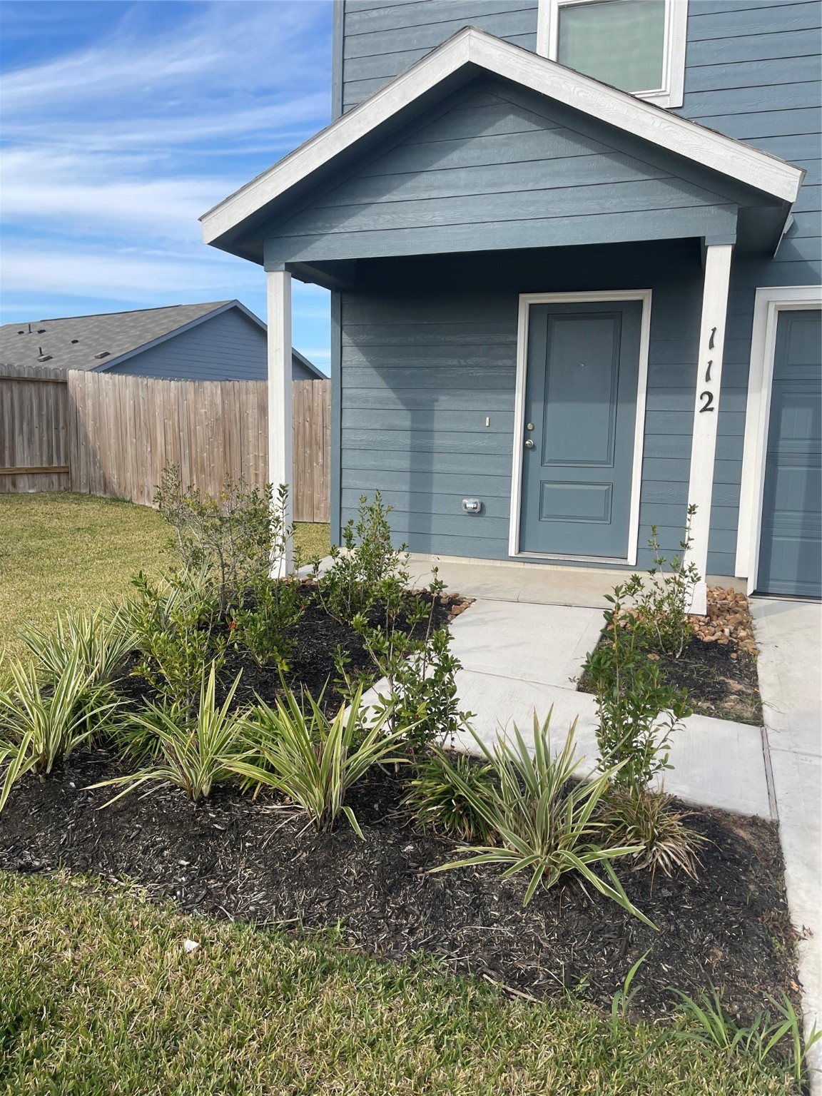112 Stran Street Wharton, TX 77488 - Photo 2 of 23 The covered entryway space is adorned with tidy garden beds, offering a sheltered and welcoming transition into the interior.