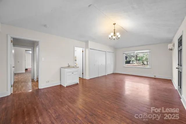 an empty room with wooden floor chandelier and windows