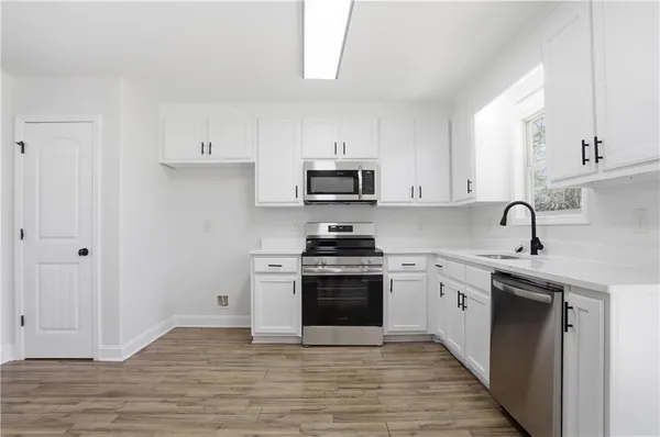 a kitchen with stainless steel appliances granite countertop a stove top oven a sink and white cabinets
