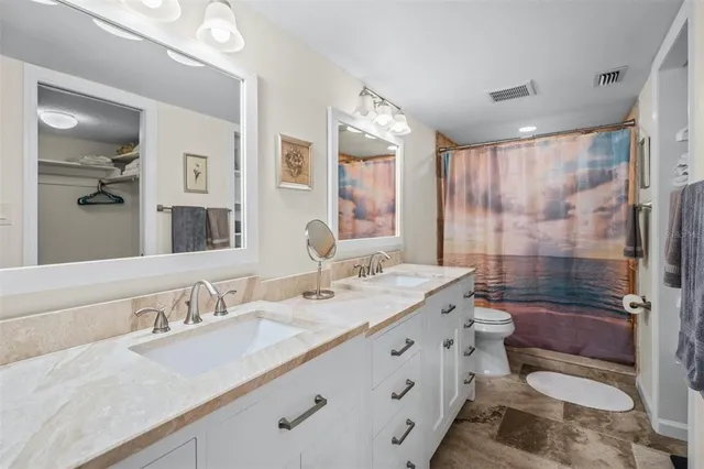 a bathroom with a granite countertop double vanity sink toilet mirror and shower