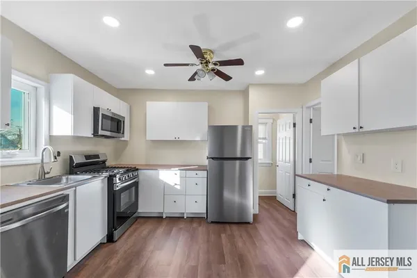 a kitchen with stainless steel appliances a refrigerator a stove top oven a sink a refrigerator and white cabinets with wooden floor