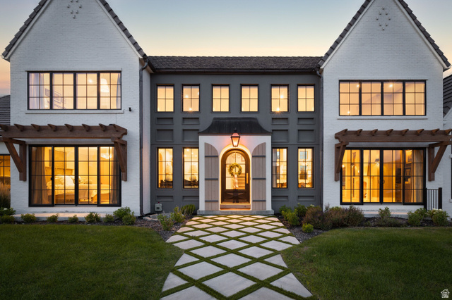 558 West Rheinfalls Circle Midway, UT 84049 - Photo 53 of 61 Modern Farmhouse estate showcasing a symmetrical facade with white and charcoal exterior finishes, multiple multi-pane windows with warm interior lighting, gabled rooflines with decorative trim details, a centered arched entryway with lantern sconce, and