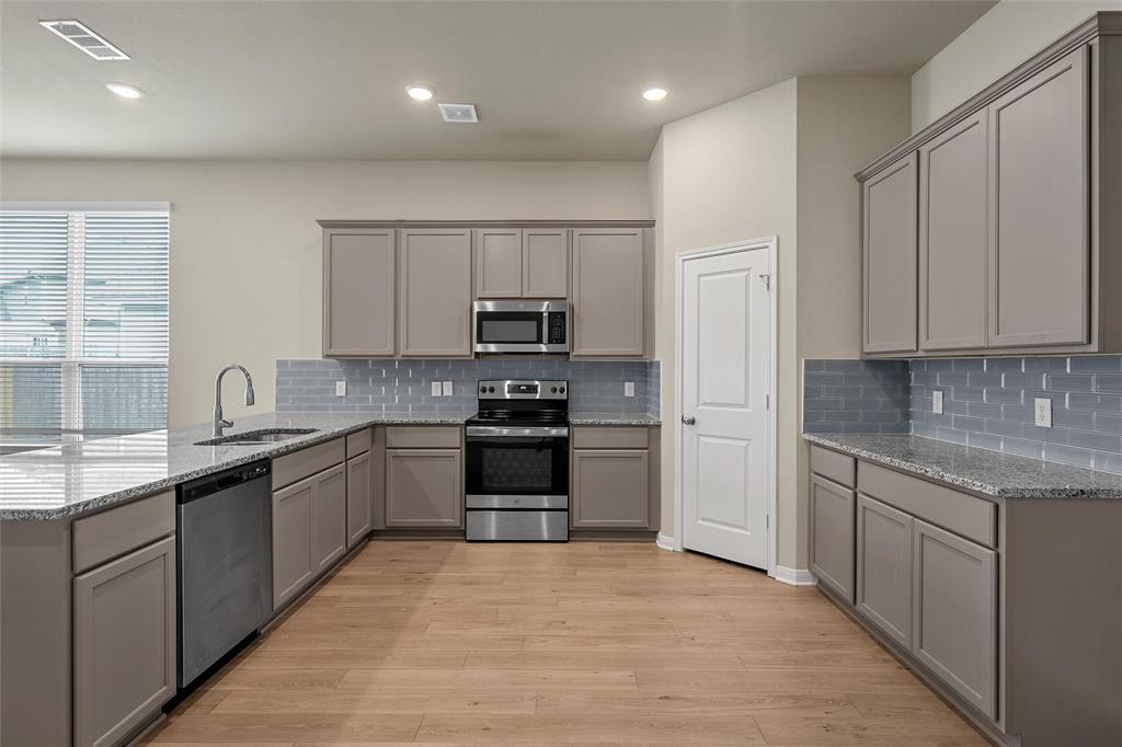 3205 Dottavio Road Lorena, TX 76655 - Photo 11 of 33 Modern kitchen featuring light wood-finish flooring, grey cabinetry, stainless steel appliances, granite countertops, and a subway tile backsplash
