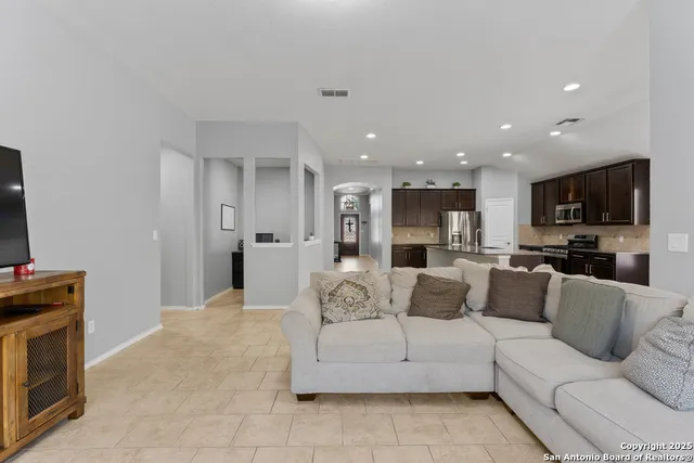 a view of a living room kitchen with stainless steel appliances kitchen island granite countertop lots of white cabinets