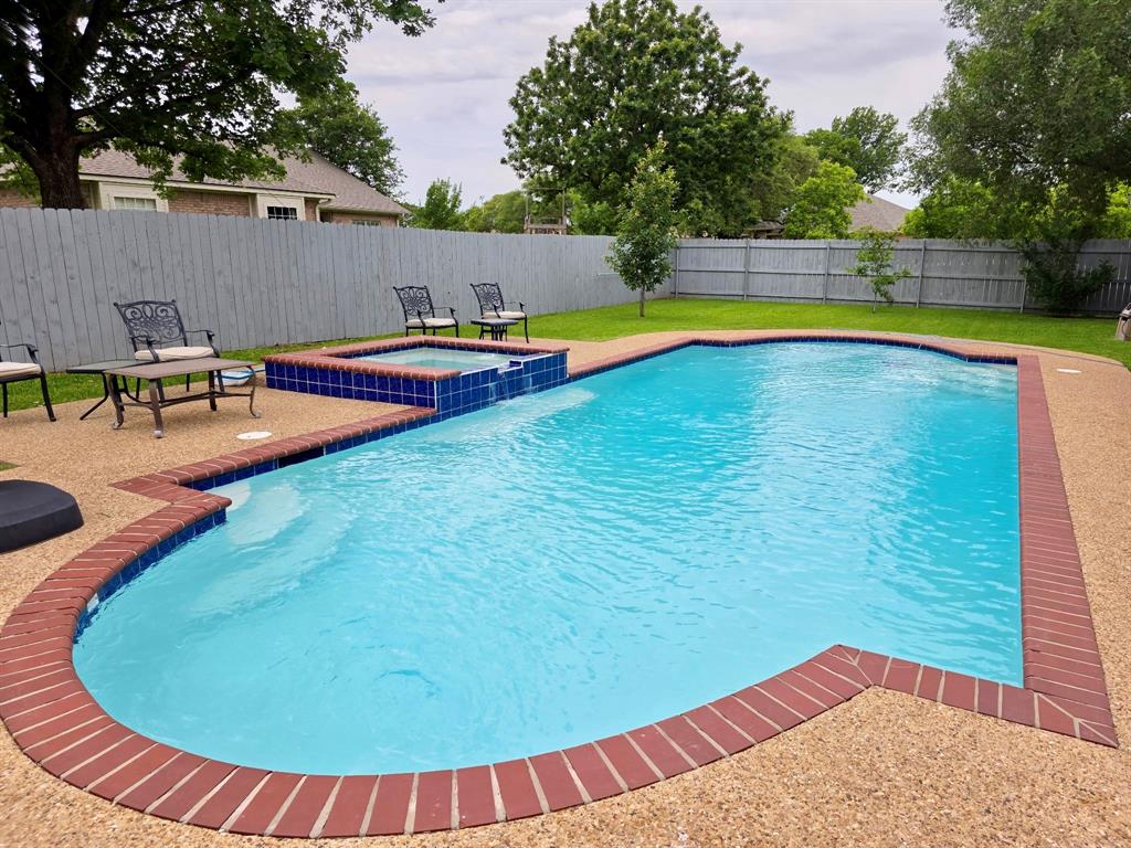 520 Red River Road Belton, TX 76513 - Photo 34 of 36 Freeform swimming pool with a connected hot tub featuring blue tile accents, surrounded by exposed aggregate concrete decking and a red brick coping