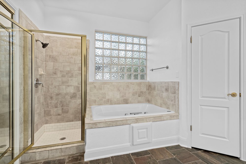 1815 Rue De St Tropez Austin, TX 78746 - Photo 32 of 40 Spacious bathroom featuring a glass-enclosed shower with tile surround, a built-in soaking tub, and a glass block window