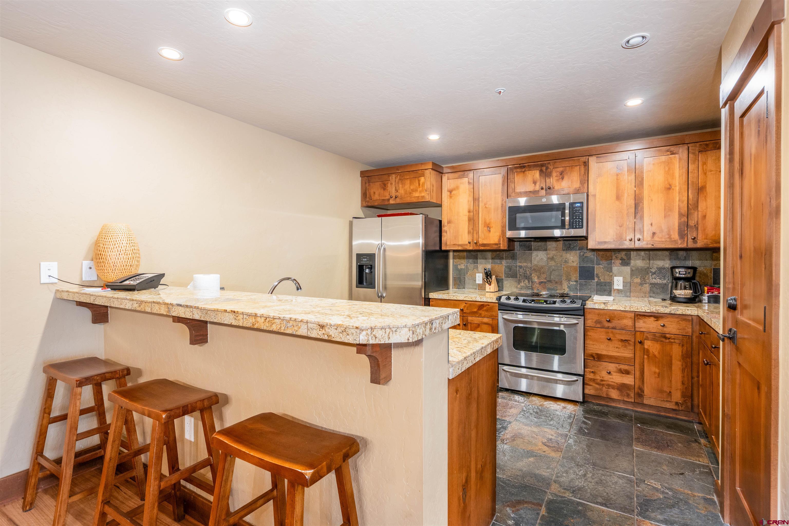 24 Sheol Street, Unit 204 Durango, CO 81301 - Photo 5 of 29 a kitchen with stainless steel appliances granite countertop a stove top oven a sink dishwasher and a refrigerator with wooden cabinets