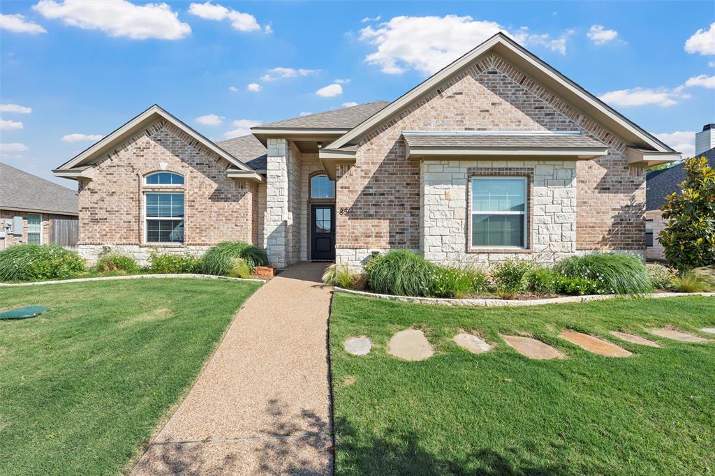 French country inspired facade featuring a front yard, stone siding, brick siding, and roof with shingles