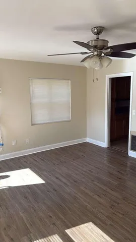 an empty room with wooden floor fan and windows