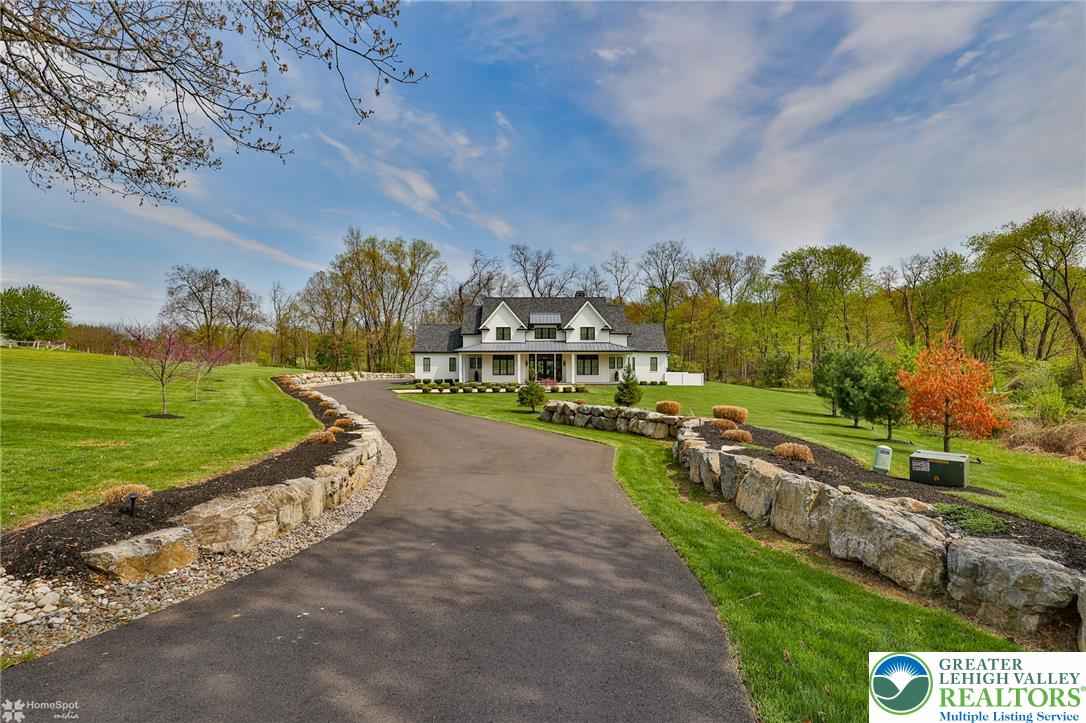 A long, curving driveway leads to a classic white residence, nestled amidst verdant lawns and mature trees.