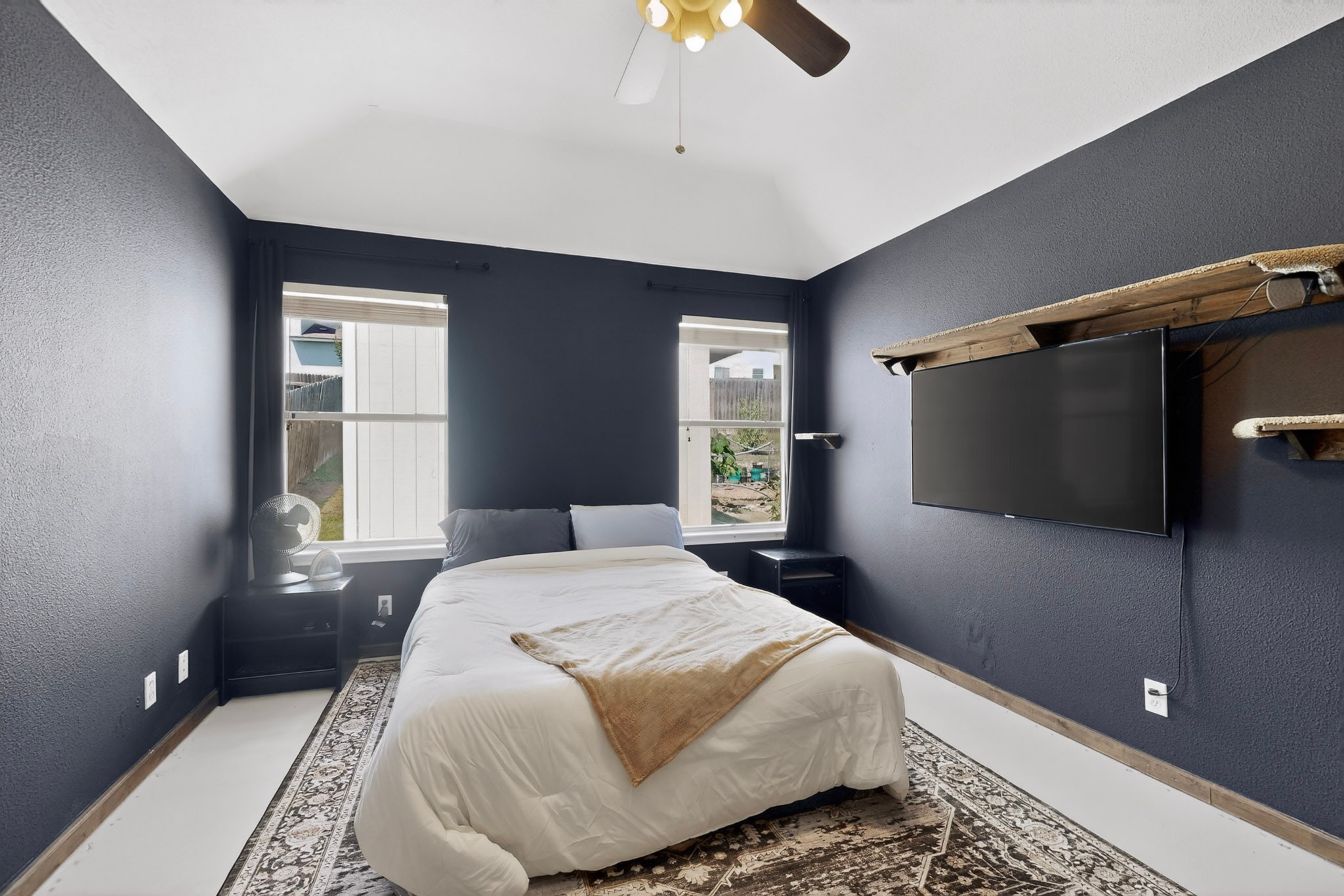 15104 Mimebark Way Austin, TX 78724 - Photo 18 of 38 Vaulted ceiling bedroom featuring two windows with exterior views, dark accent walls, a ceiling fan with integrated lighting, and a built-in media shelf