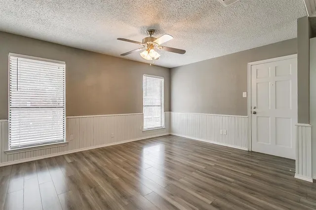 an empty room with wooden floor chandelier fan and windows