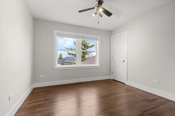 an empty room with wooden floor chandelier fan and windows