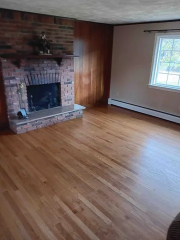 an empty room with wooden floor fireplace and windows
