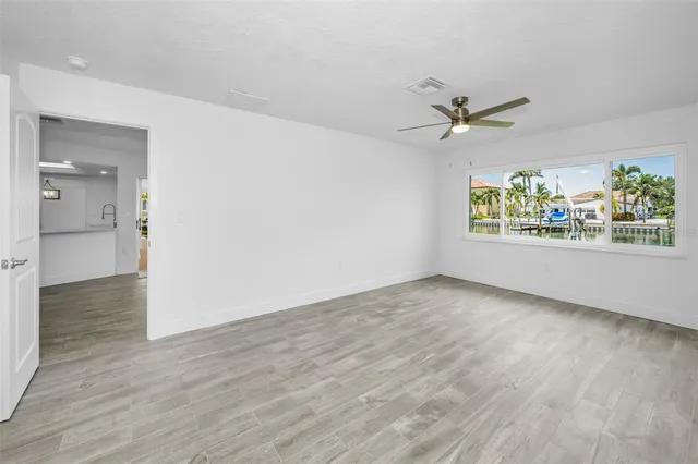 an empty room with wooden floor chandelier fan and windows