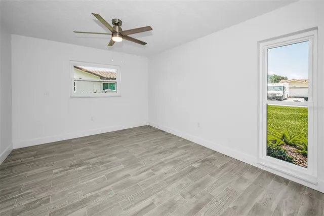 a view of an empty room with wooden floor and a ceiling fan