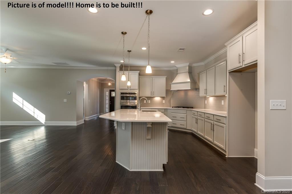 2061 New Style Way, Unit 30 Tega Cay, SC 29708 - Photo 26 of 40 a kitchen with kitchen island a sink a stove a refrigerator and white cabinets with wooden floor
