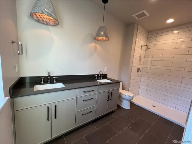 a bathroom with a double vanity sink a toilet and shower