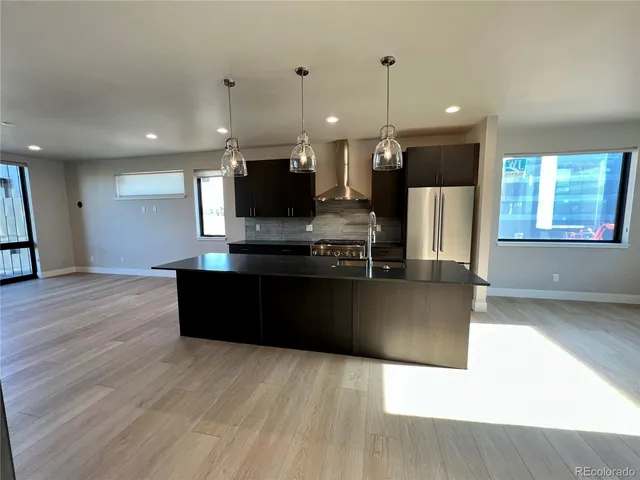 a kitchen with stainless steel appliances kitchen island granite countertop a refrigerator a stove and a wooden floor