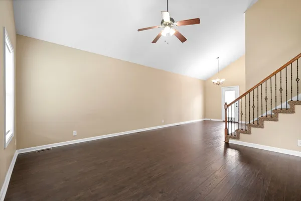 a view of an empty room with wooden floor and a ceiling fan