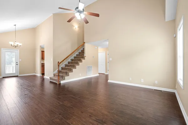 a view of an empty room with wooden floor and a ceiling fan