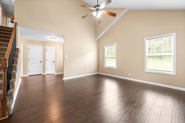 an empty room with wooden floor chandelier fan and windows