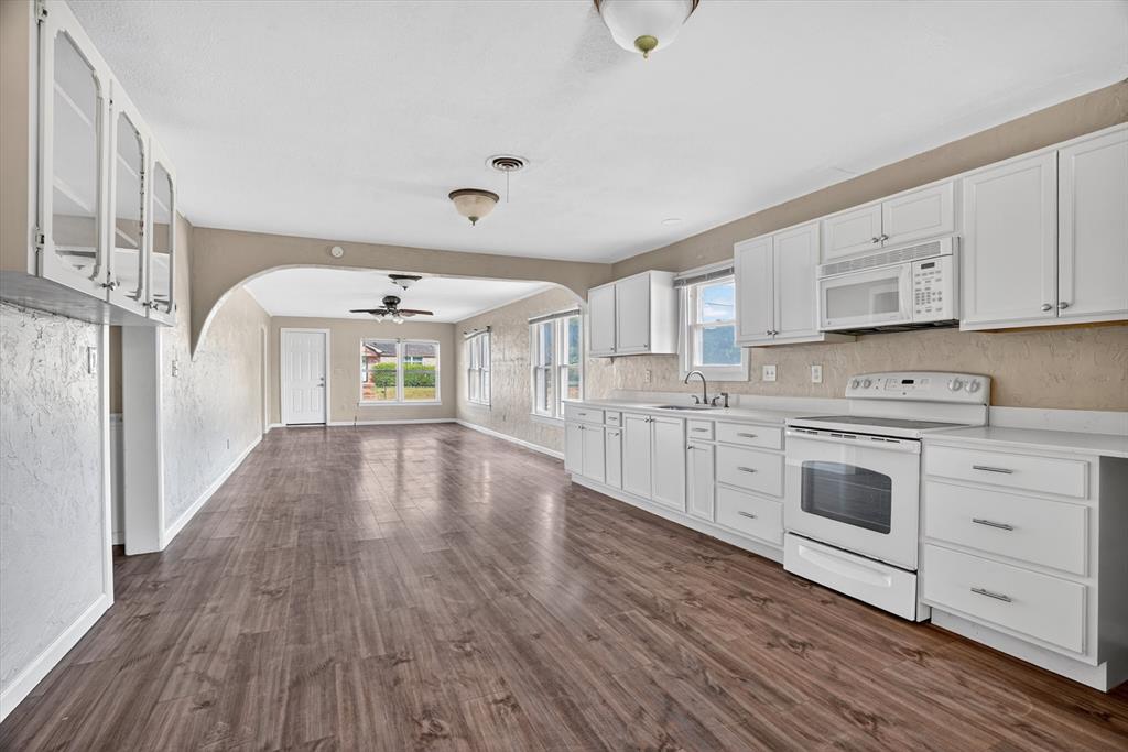 320 North 2nd Street Jacksboro, TX 76458 - Photo 3 of 16 a kitchen with stainless steel appliances a white stove top oven and white cabinets with wooden floor