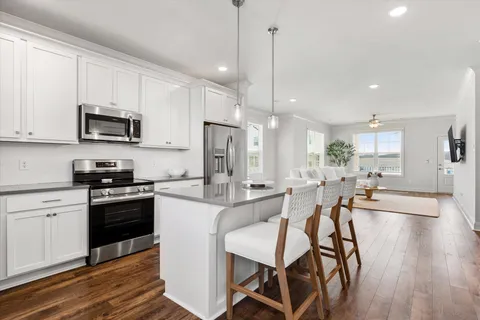 a kitchen with stainless steel appliances kitchen island granite countertop a stove a sink a microwave a refrigerator and white cabinets with wooden floor