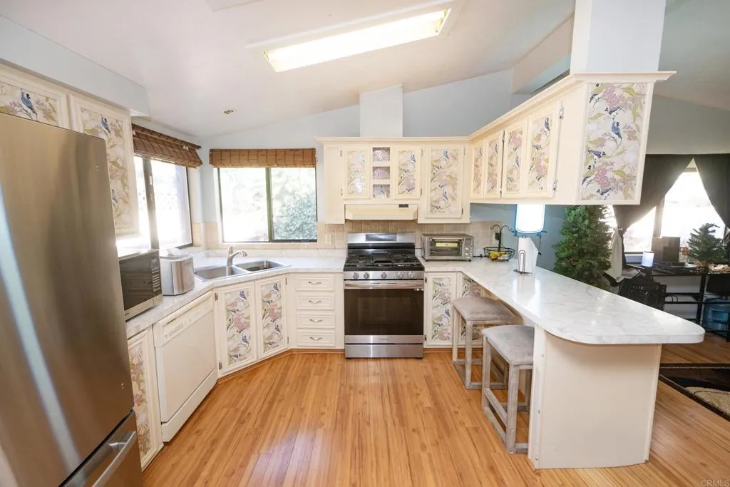 a kitchen with stainless steel appliances a stove a sink a refrigerator and white cabinets with wooden floor
