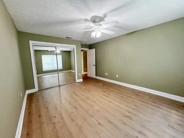 an empty room with wooden floor fan and windows