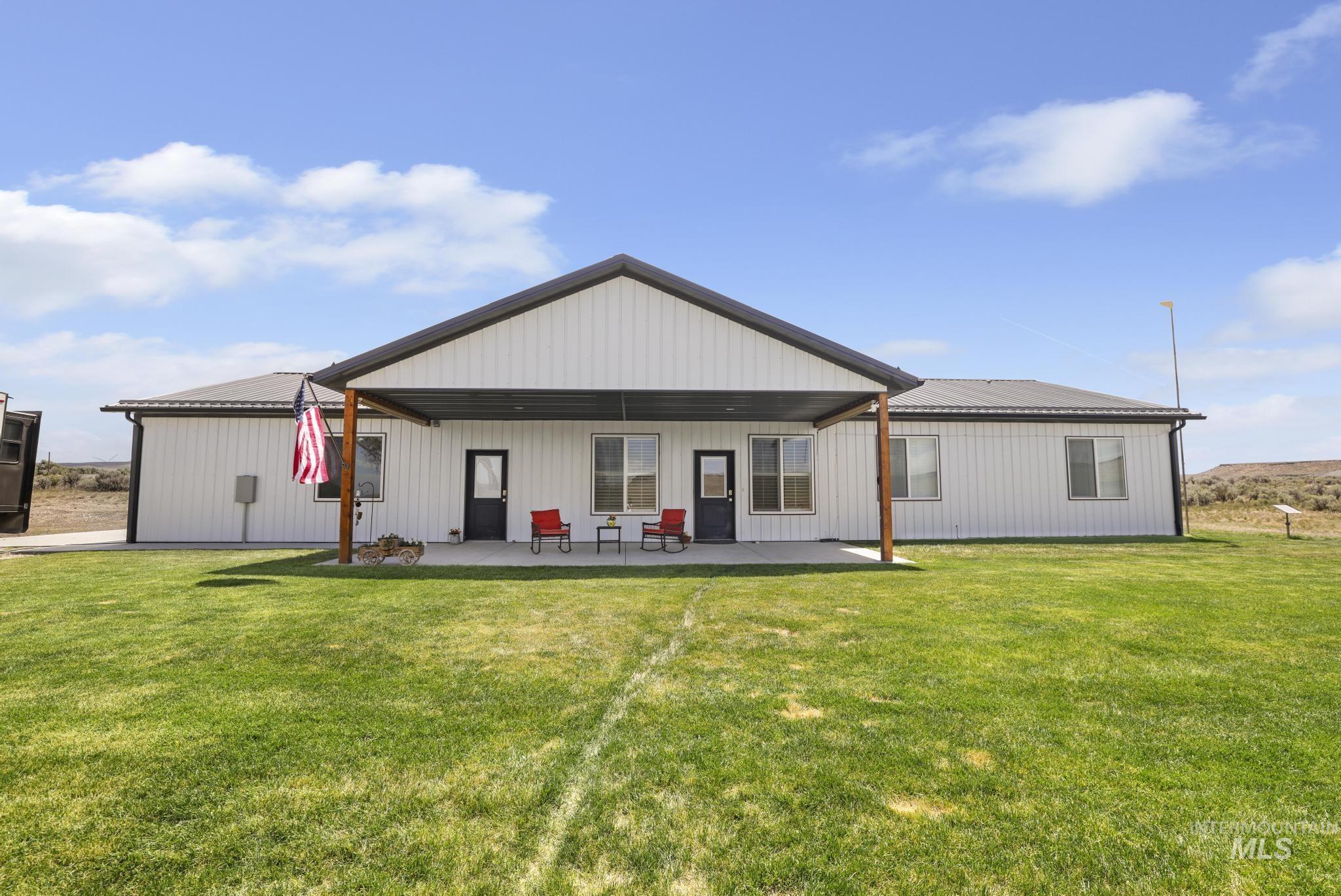 Expansive backyard with a covered patio, multiple windows, and a wide lawn