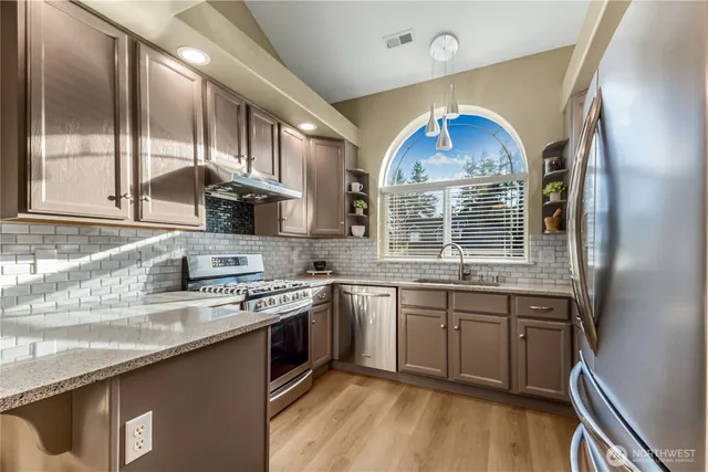 a kitchen with stainless steel appliances granite countertop a sink a stove a refrigerator cabinets and a window