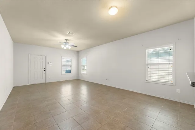 an empty room with chandelier fan and windows