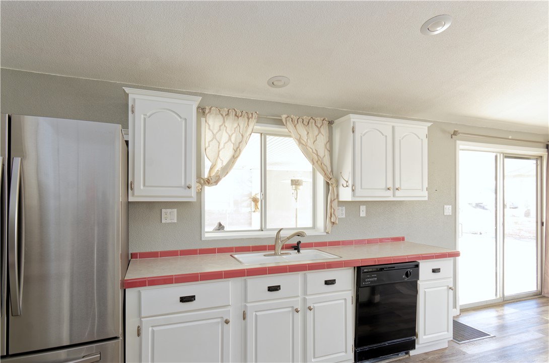 49603 Rainbow Avenue Quartzsite, AZ 85346 - Photo 16 of 44 Kitchen featuring freestanding refrigerator, tile countertops, white cabinets, black dishwasher, and light wood finished floors