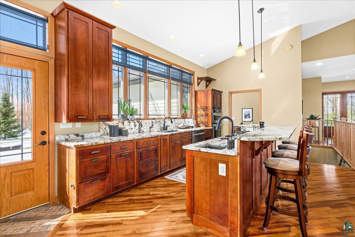 92598 Spells Road Sturgeon Lake, MN 55783 - Photo 28 of 60 Kitchen with a kitchen bar, light stone countertops, decorative light fixtures, light wood-type flooring, and vaulted ceiling