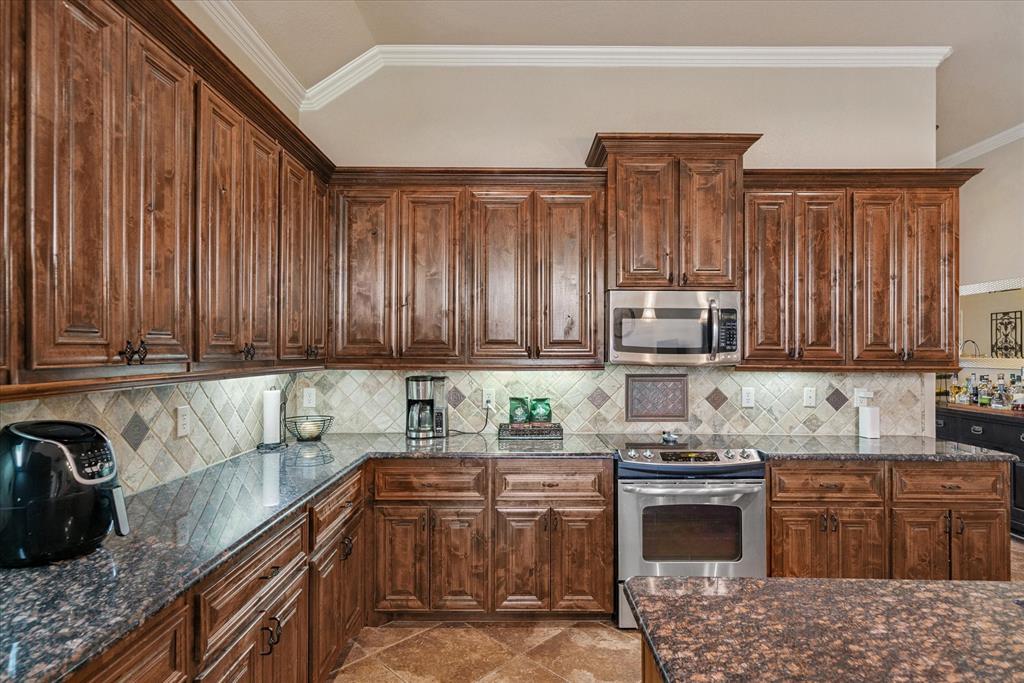 1007 Somerset Circle Forney, TX 75126 - Photo 32 of 34 a kitchen with stainless steel appliances granite countertop a stove a sink dishwasher and a microwave oven with wooden cabinets