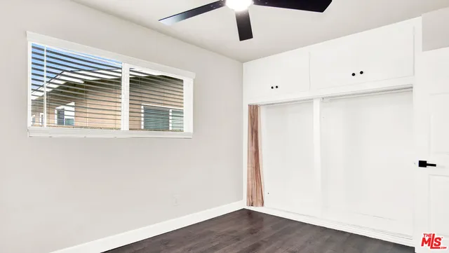 an empty room with wooden floor ceiling fan and window