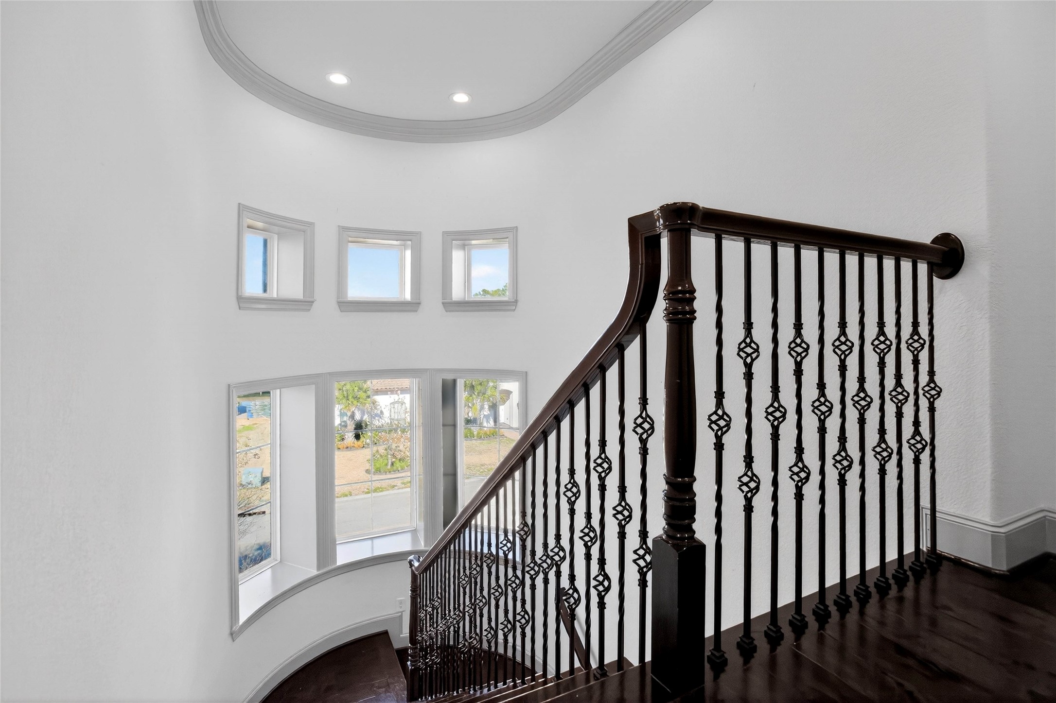 12349 Tramonto Conroe, TX 77304 - Photo 29 of 50 This photo showcases a beautifully designed staircase (view from third floor) with elegant dark wood railings and intricate iron balusters. The space is brightened by a series of large windows, offering a modern and airy feel.