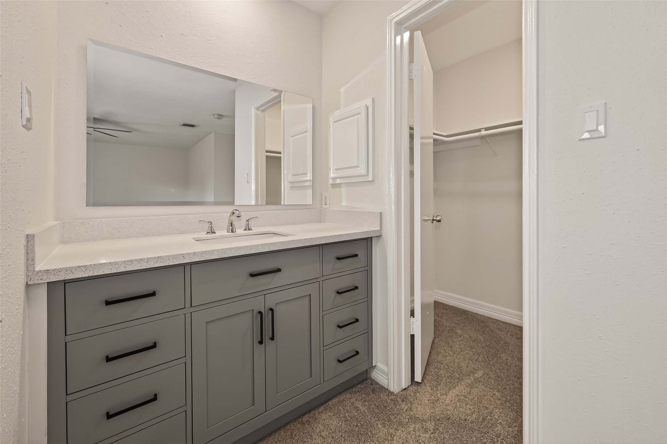 7027 Dickson Way Missouri City, TX 77489 - Photo 16 of 22 This photo showcases a modern bathroom vanity with a large mirror and ample storage in sleek gray cabinetry. Adjacent is a walk-in closet with carpeted flooring, providing a convenient and functional space.