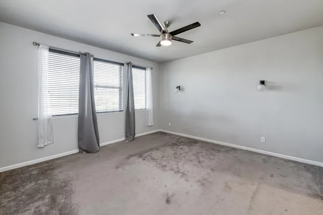 an empty room with ceiling fan and windows