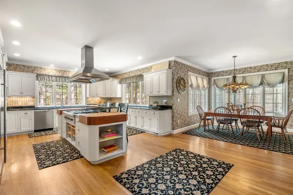 a kitchen with stainless steel appliances kitchen island granite countertop a stove top oven a sink a dining table and chairs with wooden floor