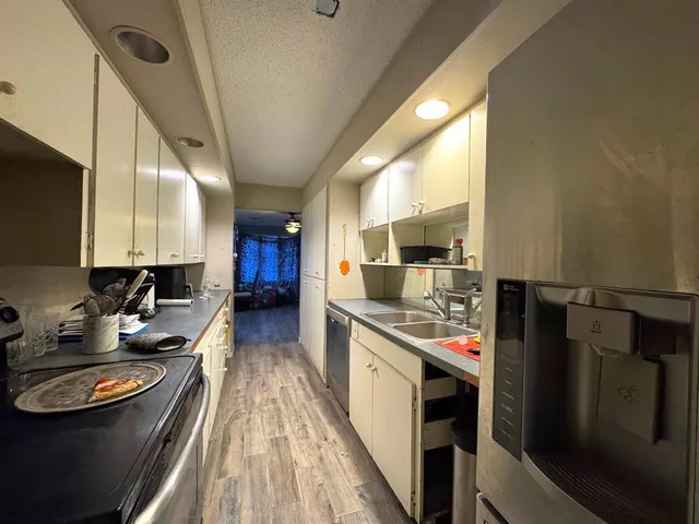 a kitchen with stainless steel appliances a stove a sink dishwasher a refrigerator white cabinets and wooden floor