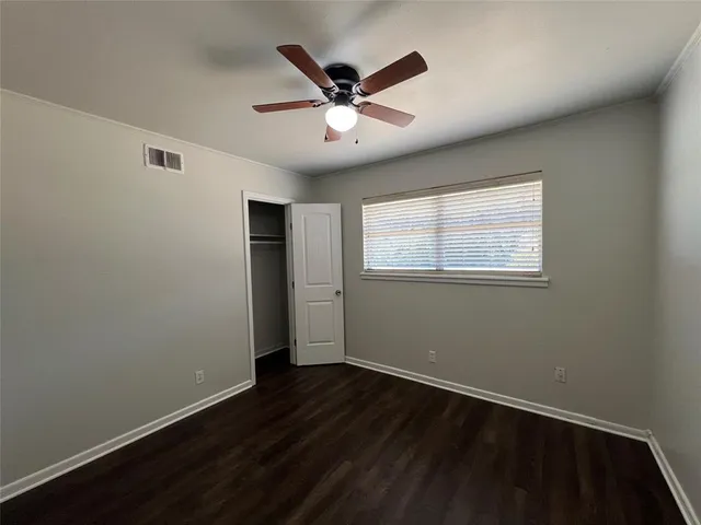 a view of an empty room with wooden floor and a ceiling fan